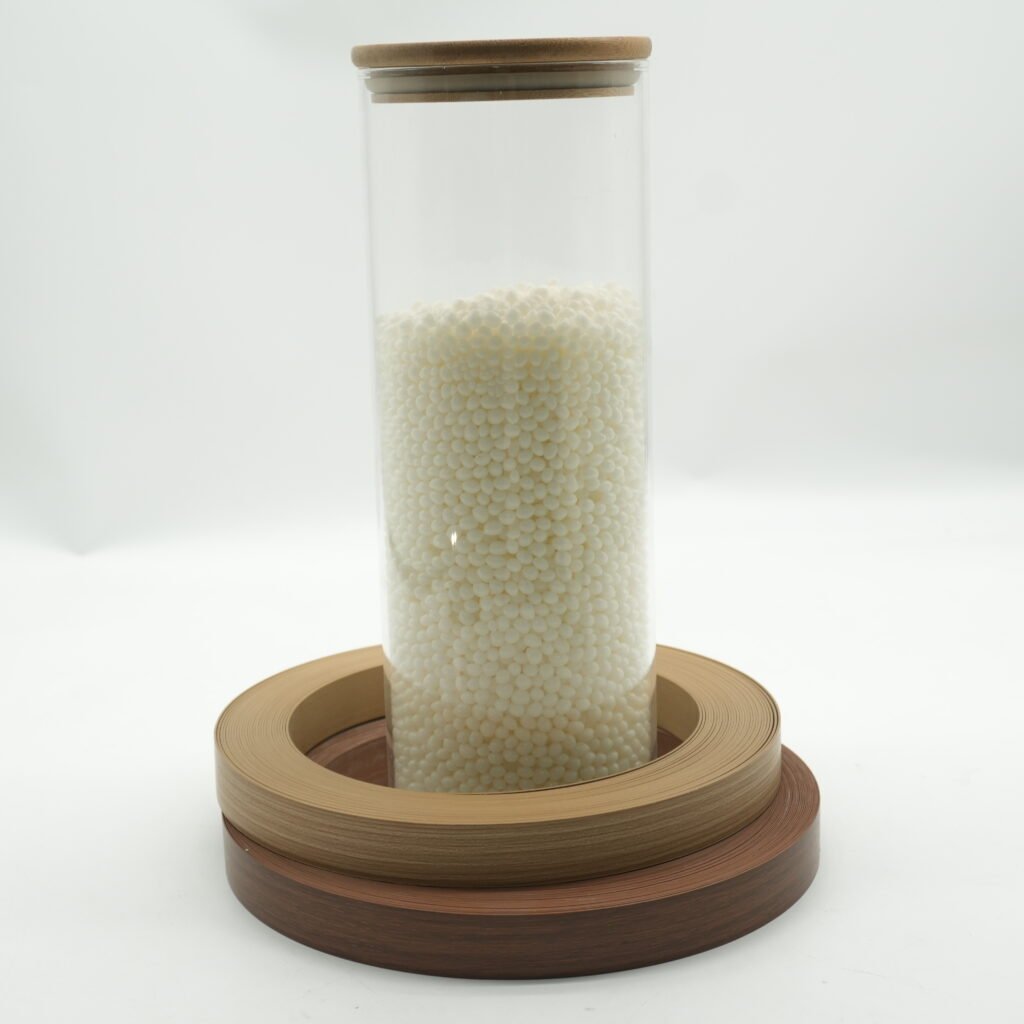 Sample jar filled with glue for edge banding hot melt granules beside edge banding rolls